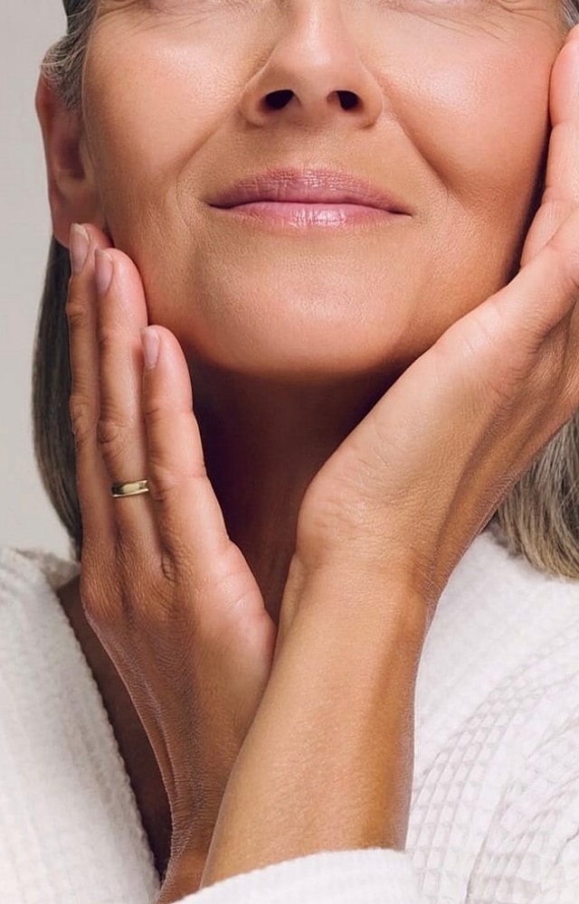 Woman gently touching her face, smiling.