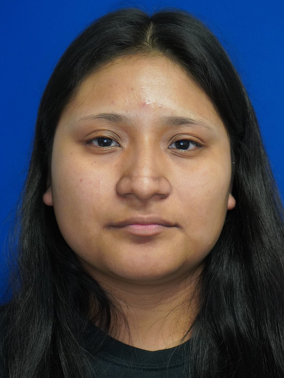 Young woman with long black hair, neutral expression.
